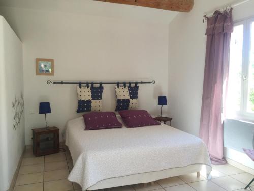 a bedroom with a bed with purple pillows and a window at Les Restanques in Goult