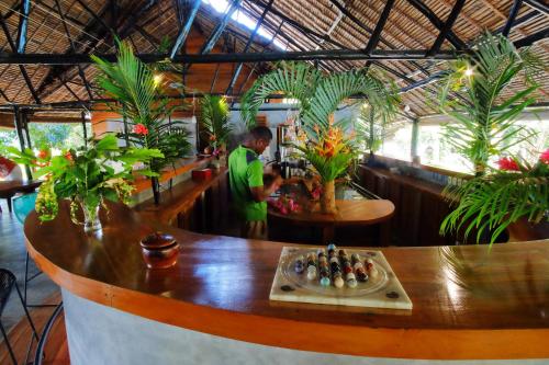 a man standing at a counter in a restaurant with plants at L'heure Bleue in Ambatoloaka