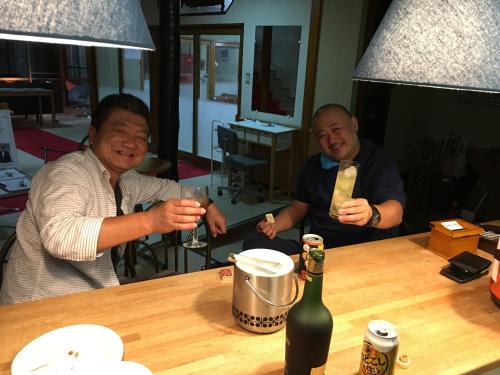 two men sitting at a table with a bottle of wine at Towadako Hostel in Towada