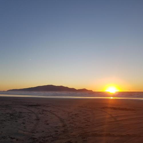 una puesta de sol en la playa con una montaña en el fondo en Near the shore en Waikanae