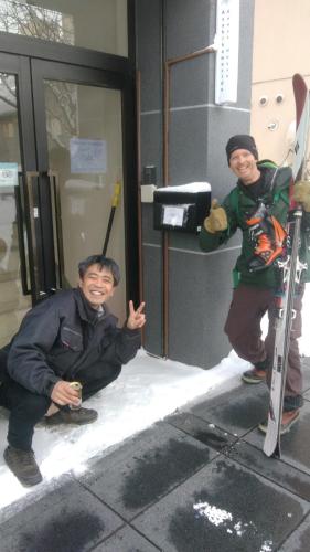 two men sitting on the snow outside of a building at Asahikawa Ride in Asahikawa