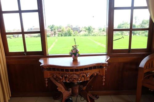 einen Holztisch in einem Zimmer mit Fenstern in der Unterkunft Ganesha Ubud Inn in Ubud