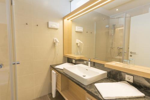 ein Bad mit einem Waschbecken, einer Dusche und einem Spiegel in der Unterkunft Strandhotel Kärntnerhof in Pörtschach am Wörthersee