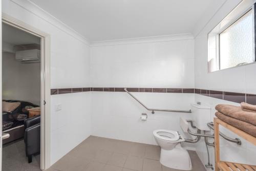 a white bathroom with a toilet and a window at Moore Park Beach Inn in North Coast