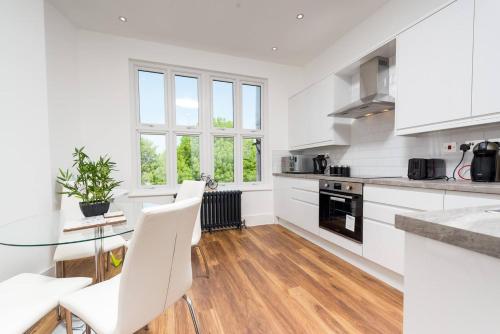 uma cozinha branca com uma mesa de vidro e cadeiras brancas em Stunningly Luxurious London Apartment (MHB350) em Londres