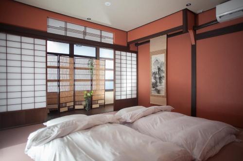 a bed in a room with orange walls and windows at Oyama TABI-NE in Kanazawa