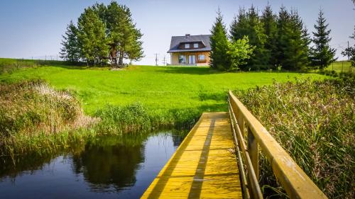 a wooden bridge over a river with a house in the background at Dom w Głuszynie z linią brzegową in Głuszyn