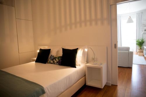 a bedroom with a bed with white sheets and black pillows at Apartamentos Praça Amarela by Heart of Funchal in Funchal