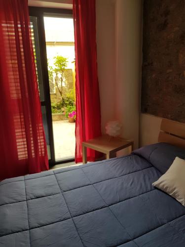 タオルミーナにあるCasa Auroraのベッドルーム1室(ベッド1台付)、赤いカーテン付きの窓が備わります。
