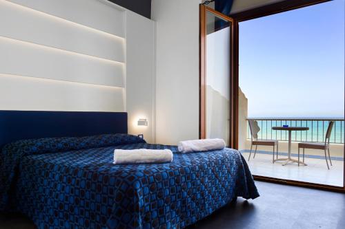 a hotel room with two beds and a table and a balcony at Hotel La Battigia in Alcamo Marina