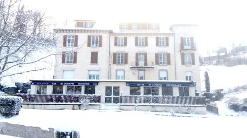 un gran edificio con nieve en el suelo delante de él en Hôtel St Joseph en Vic-sur-Cère