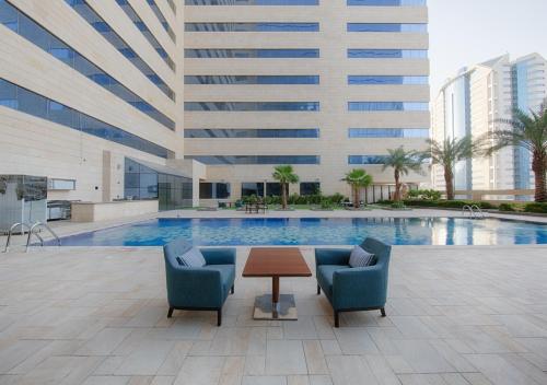 a pool with two chairs and a table and a building at Holiday Suites Al Azizia in Makkah