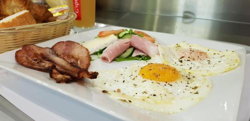 a plate of food with eggs bacon sausage and bread at Hotel Le Paris in Noumea