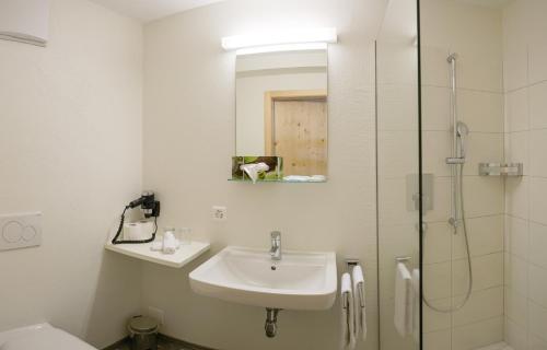 a white bathroom with a sink and a shower at Hotel Steinbock Vals in Vals