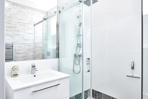uma casa de banho branca com um chuveiro e um lavatório. em Apartamenty Między Jeziorami em Olsztyn