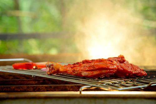 a chicken is cooking on a grill with carrots at Spice Villa Thekkady in Thekkady