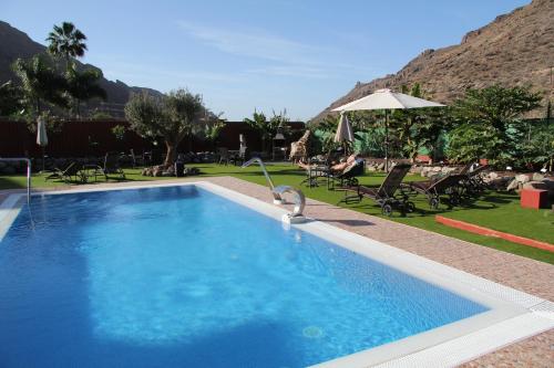 a swimming pool in a yard with chairs and umbrellas at Sol Mogan Suites - Adults Only in Puerto de Mogán