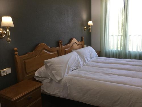 a bedroom with a bed with white sheets and a window at Hotel Cinco Castaños in Candelario