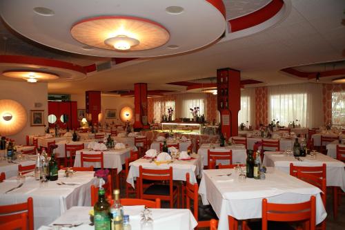 un comedor con mesas blancas y sillas rojas en Hotel Venezia e la Villetta, en Lido di Jesolo