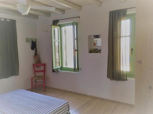 1 dormitorio con paredes blancas, ventanas verdes y silla roja en Serifos Vacation Home en Rámos