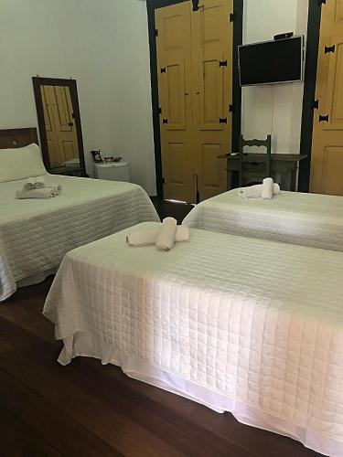 two beds in a hotel room with white sheets at Pousada Vovô Chiquinho in Tiradentes