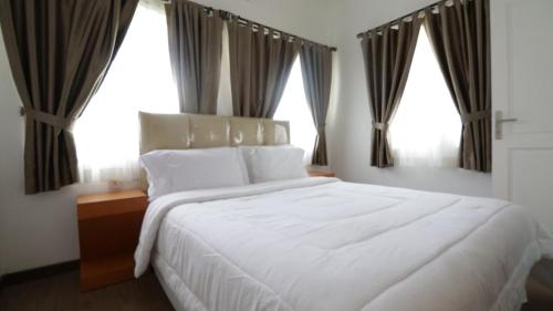 a bedroom with a large white bed with windows at Diyar Villas Puncak F4/8 in Puncak
