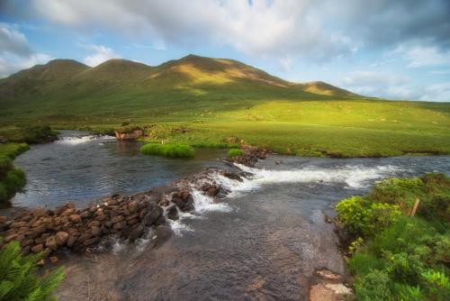 a river with rocks and mountains in the background at Wild Atlantic Hostel in Leenaun