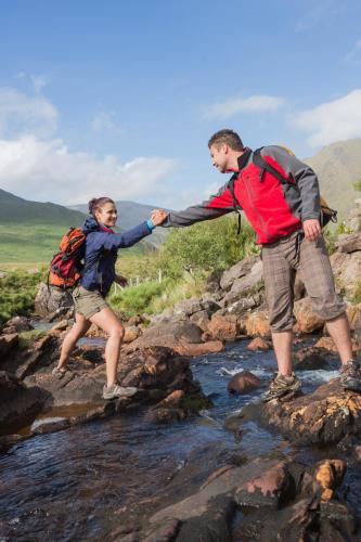 a man and a woman crossing a stream at Wild Atlantic Hostel in Leenaun