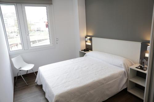 a white bedroom with a white bed and a chair at Pensión Rúa Peregrino in Sarria