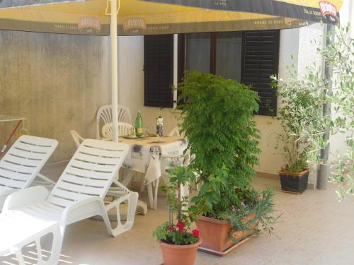 une terrasse avec des chaises blanches, un parasol et des plantes dans l'établissement Apartment Artusi, à Pula