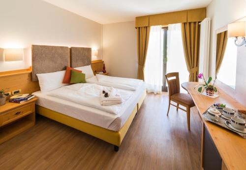 a bedroom with a bed with a desk and a chair at Hotel Ambassador in Levico Terme