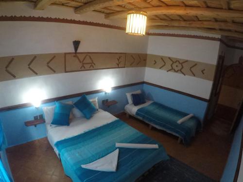 a bedroom with two beds with blue pillows and a table at Auberge des peupliers Café Restaurant in Akhendachou nʼAït Ouffi