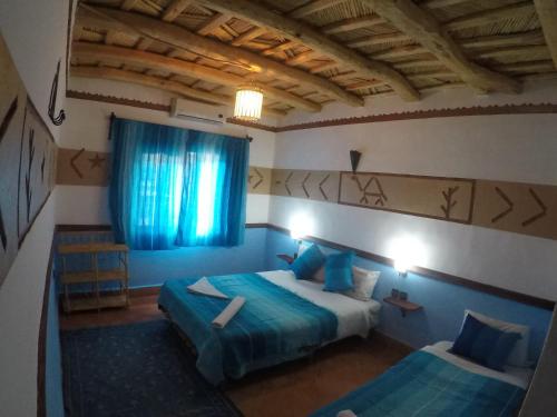 1 dormitorio con 2 camas con sábanas azules y ventana en Auberge des peupliers Café Restaurant, en Akhendachou nʼAït Ouffi