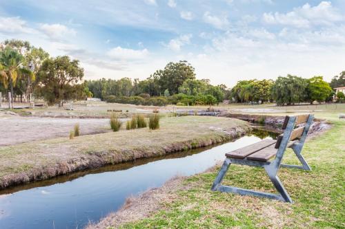 a wooden bench sitting next to a river at The Swan Valley Retreat in Henley Brook