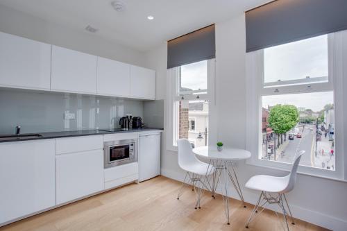 a kitchen with white cabinets and a table and chairs at Chapel Market Serviced Apartments by Concept Apartments in London