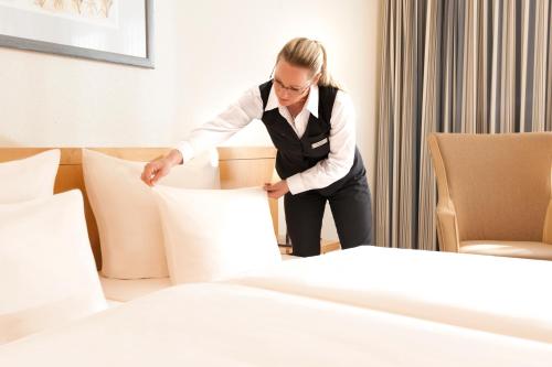 a woman in a hotel room putting pillows on a bed at Dorint Am Goethepark Weimar in Weimar