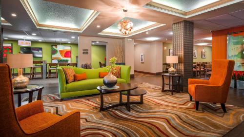 um átrio com um sofá verde e cadeiras laranja em Best Western Plus Universal Inn em Orlando