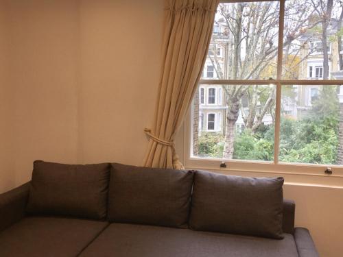 un sofá en una sala de estar con ventana en Lexham Gardens Lodge 5 en Londres