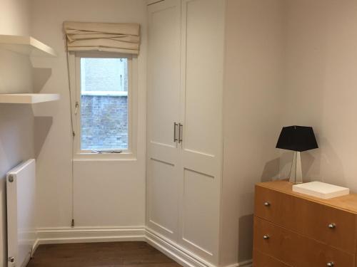 Habitación con armarios blancos, ventana y cómoda. en Lexham Gardens Lodge 5 en Londres