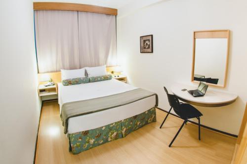 ein Schlafzimmer mit einem Bett, einem Tisch und einem Stuhl in der Unterkunft Hotel Aladdin in Curitiba