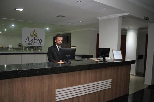 a man in a suit sitting at a counter with a laptop at Astro Palace Hotel in Uberlândia