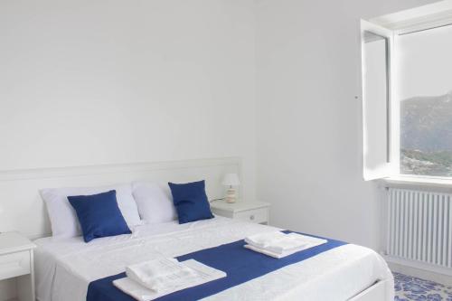 a white bed with blue pillows and a window at Angiem Holiday House Ravello in Ravello