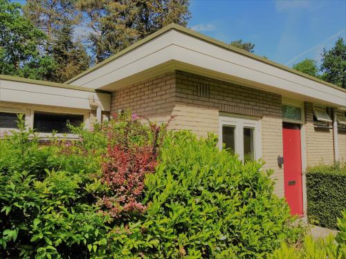 a house with a red door and some bushes at Bungalow Hartje Veluwe in Otterlo