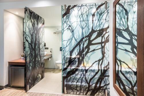 baño con puerta de cristal con un mural de árbol en SHG Bogotá 100 Design Hotel, en Bogotá