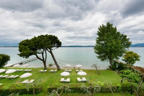 a group of white chairs and umbrellas on a lawn near the water at Hotel Saviola in Sirmione