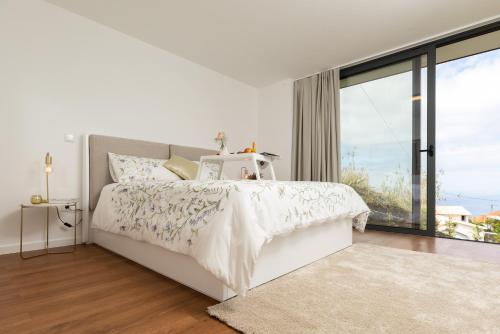 a white bedroom with a bed and a large window at Casa Melinho Lotus in Calheta