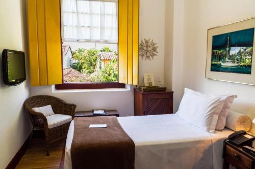 a bedroom with a bed with a window and a chair at Pousada do Ouro in Paraty