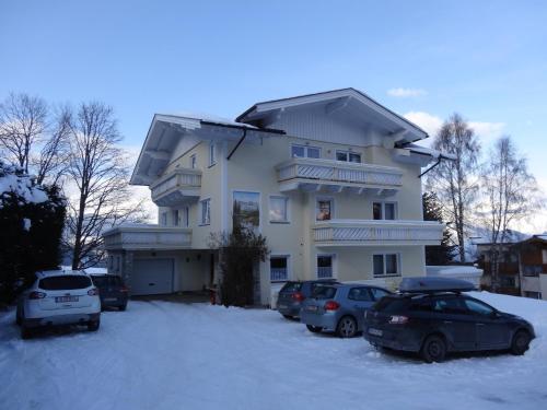 a large white house with cars parked in the snow at Haus Alpina Ski In & Ski Out in Schladming