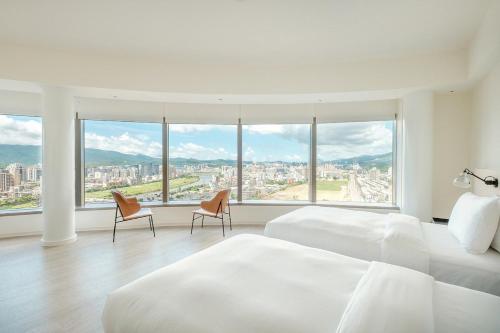 a white bedroom with two beds and two chairs at amba Taipei Songshan in Taipei