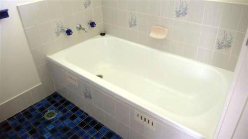 a white bath tub in a bathroom with blue tiles at BARRELS AT BOOMERANG in Blueys Beach